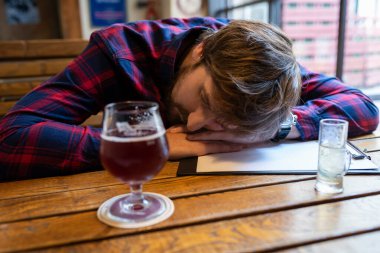 Alkolizm konsepti. Barda yalnız sarhoş bir adam bir masada uyuyor. Alkol bağımlılığı ve depresyonla mücadele