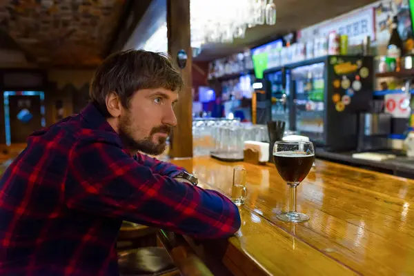A man sits alone at the bar and drinks alcohol. Sad depressed drunk guy suffering from alcohol abuse, alcoholism concept