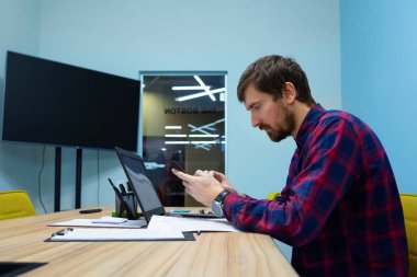 Ofiste çalışan genç işadamı ofis masasında oturuyor. İş danışmanlığı, online eğitim, yaşam tarzı, serbest çalışma. Yan görünüm.