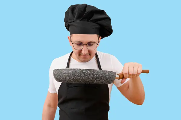 Mavi arka planda elinde tavayla bir aşçı. Yemek pişirme konsepti.
