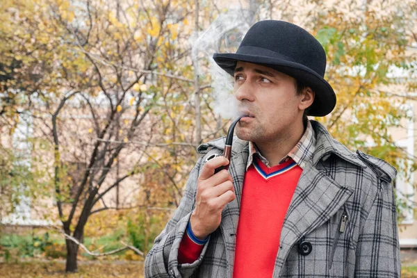 Portrait of a man smoking a pipe in a city park.