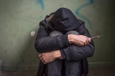 Kapüşonlu umutsuz bir bağımlının ve terk edilmiş bir evde yerde otururken çekilmiş fotoğrafı. Uyuşturucu bağımlılığı kavramı.