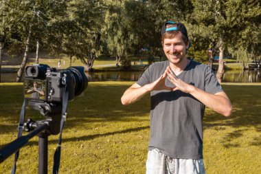 Genç bir adam güneşli bir günde parkta bir kamerada blog için video kaydediyor..