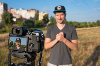 Parktaki bir erkek blogcu güneşli bir günde parktaki bir kameraya video kaydediyor. Video eğitimi, uzak bağımsız çalışma, yaşam tarzı
