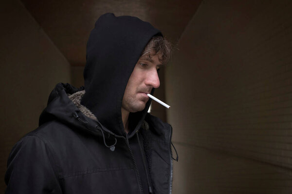 A man in a hood on the street. The concept of alcoholism and drug addiction. Depression, Unemployment, Social problems.