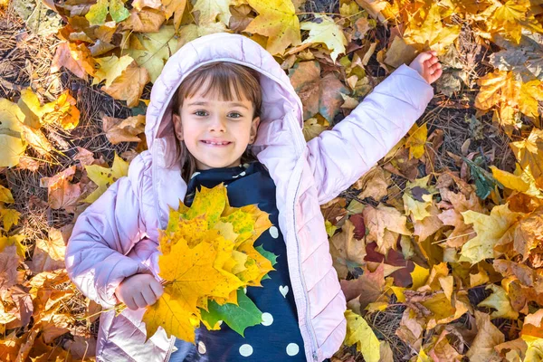 Akçaağaç yapraklı mutlu çocuk sırt üstü yatarken parkta oynar. Altın saat.