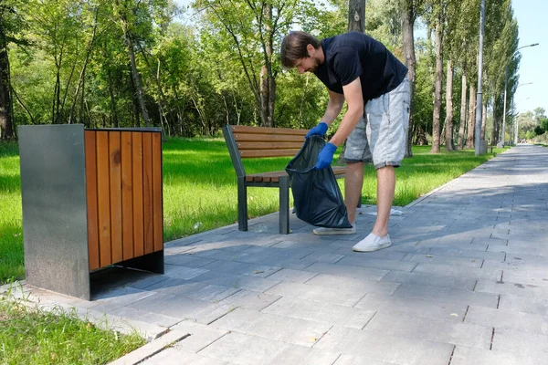 Parkta gönüllü bir erkek plastik çöpü torbaya koyuyor. Çevresel sorunlar, çevre kirliliği, doğa.