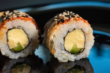 Sushi, arka planda susam tohumlarıyla birlikte yakın plan çekimde yuvarlanır. Japon yemeği..