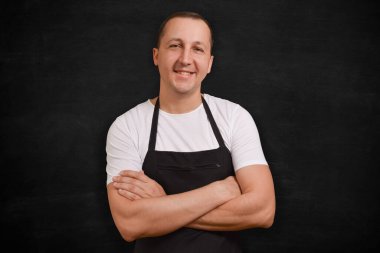 Önlüklü mutlu aşçı siyah arka plandaki kameraya bakıyor. Yemek hazırlıyorum..