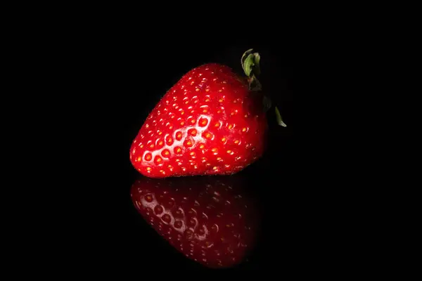 One fresh strawberry on a black background. Ripe berry
