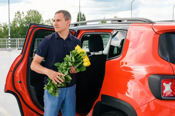 一个手里拿着花的男人站在一辆汽车旁边 — 图库照片