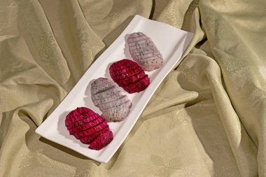 Bir tabakta kırmızı ve beyaz renkli Pitaya meyvesi.