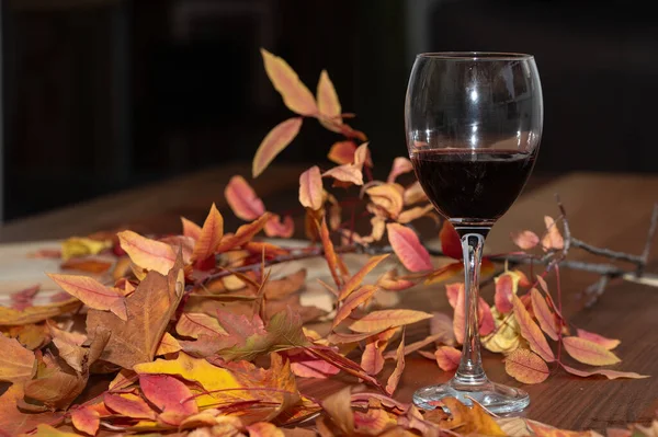 Yellow and red autumn leaves on a wooden floor, red wine in a glass.