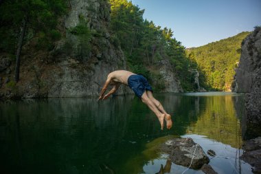 Ormanlarla çevrili bir göle atlayan bir adam. Karacaoren Baraj Gölü.
