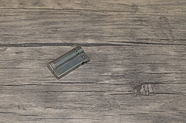 Old petrol metal lighter on wooden floor.