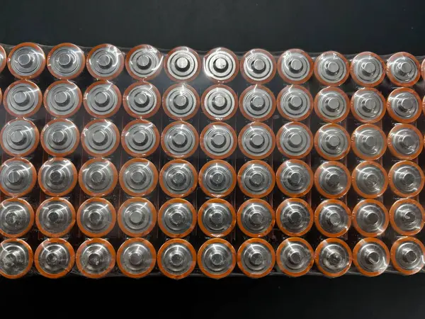 Multiple used AA alkaline batteries are seen in a pile. Close-up front view from the plus side of the battery.