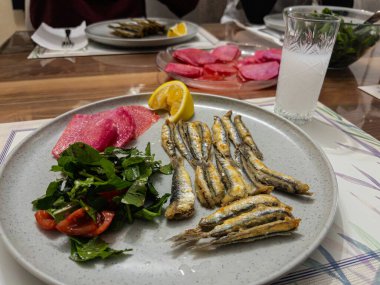 Kızarmış balık, salata ve ahşap bir masada bir tabak kırmızı turp dilimleri. Bir bardak Türk rakısı..
