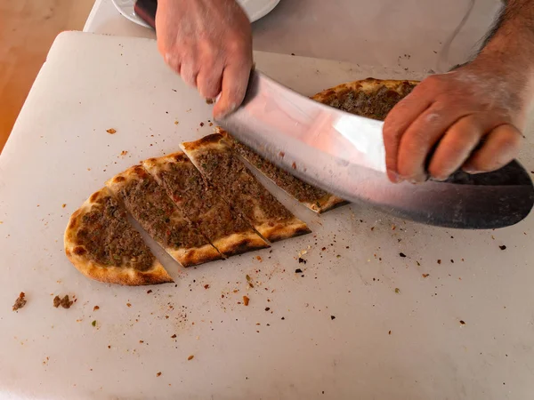 A man slicing a mince pita baked in the oven.