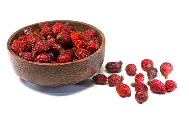 Beyaz arka planda, ahşap kasenin içinde ve dışında izole edilmiş gül çilekleri..