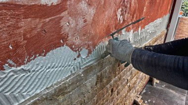 Dairedeki tamirat: Duvara taş koymak. Bir işçi duvarı yapıştırıcı ile kaplamak için mala kullanır..