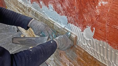 Dairedeki tamirat: Duvara taş koymak. Bir işçi duvarı yapıştırıcı ile kaplamak için mala kullanır..