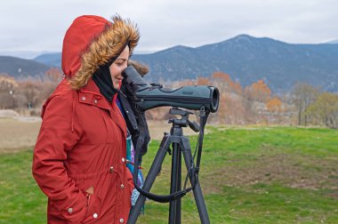 Göl kenarında teleskopla izleyen kırmızı ceketli genç kız..