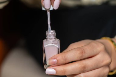 Kız ojeyi pembe bir oje şişesinden fırçayla çıkarıyor..