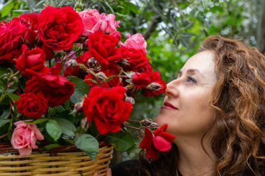 Elinde bir sepet kırmızı ve pembe gül tutan mutlu bir kadın..