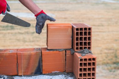 İşçi ev inşaatı için tuğla duvar örüyor. Havan topu kullanarak tuğla duvar ören bir işçi. İnşaat alanına tuğla döşeyen duvarcılara yakın çekim. Tuğlalı işçi.