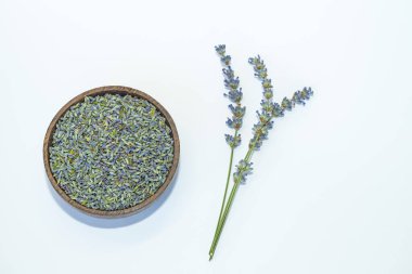 Beyaz arka planda, bir kasede, kurutulmuş lavanta çiçekleri ve taze lavanta filizi..