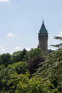 Clock tower in Luxembourg city centre behind green trees. Blue sky background. clipart