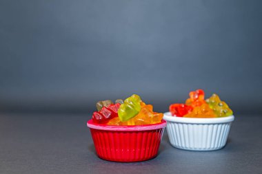 Küçük kaselerde renkli ve küçük jel şekerler. Gri zemin ve arka plan.