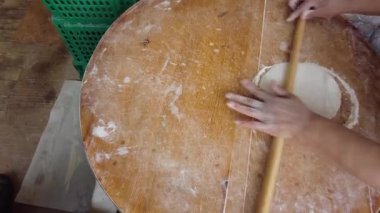 Türk usulü ekmek yapan bir kadın, hamuru tahtaya sarılmış bir iğneyle yuvarlıyor..