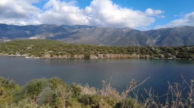 Mavi ve beyaz bulutlu gökyüzü, dingin bir göl ve dağlar. Beymelek, Antalya, Türkiye.