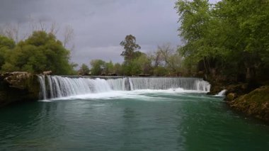 Bulutlu bir kış gününde yeşil ağaçların arasında şelale. Manavgat Şelalesi, Türkiye.