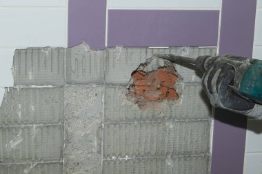 Zanaatkar elektrikli bir hilti ile duvarı yıkıyor. Usta bir evi dekore ediyor..
