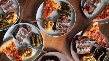 Tahta bir masada tabakta servis yapmaya hazır çeşitli yiyecekler. Pasta, hamur işleri, pizza dilimleri ve geleneksel Türk yemeği sarması..