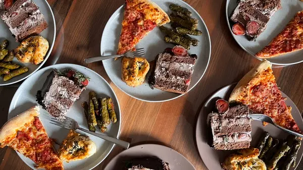 Tahta bir masada tabakta servis yapmaya hazır çeşitli yiyecekler. Pasta, hamur işleri, pizza dilimleri ve geleneksel Türk yemeği sarması..