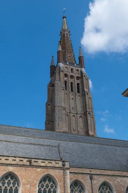 Uzun Gotik kilise kulesi, taş işçiliği ve sivri kemerleriyle, tarihi Bruges 'deki parlak mavi gökyüzüne gururla karşı duruyor..