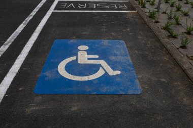 Engelli park alanı, üzerinde beyaz tekerlekli sandalye sembolü ve asfaltında RESERVED yazan mavi bir kare ile gösterilir. Bu, kentsel planlamada erişilebilirliğin ve dahil olmanın önemini vurgular..