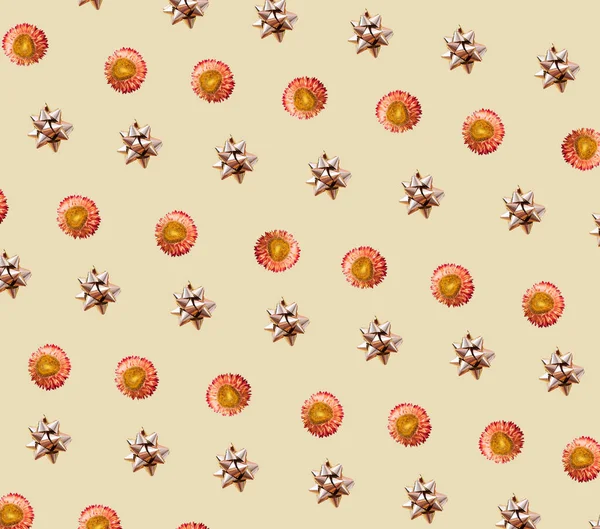 Abstract repetitive pattern composition made by glitter silver self adhesive bow and beautiful yellow and orange petal flower. Aesthetic concept on light yellow or beige background.