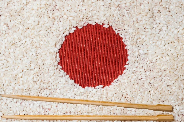 Beyaz arka plan olarak pirinç ve kırmızı tekstil dairesiyle yapılmış basit bir sanat konsepti. Geleneksel ahşap çubuklu suşi yemeği ile Japon bayrağı
