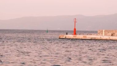 Rijeka 'daki deniz manzarasının sabah statik görüntüleri. Limandaki iskelede kırmızı bir deniz feneri. Uçan bir martı ve deniz dalgaları tarafından taşınan yeşil bir seyir şamandırası.. 