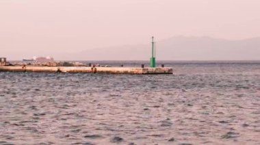 Rijeka 'daki deniz manzarasının sabah statik görüntüleri. Limandaki iskelede yeşil bir deniz feneri ve arka planda konteynır gemileri var. Rüzgarlı bir hava nedeniyle deniz dalgalanmaları gösterir. 