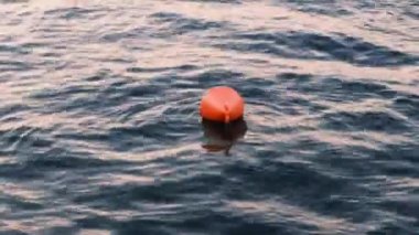 Limanda sabahın erken saatlerinde deniz dalgası yüzeyinde turuncu plastik bir şamandıra. Güneşin doğuşunda rüzgarlı su.