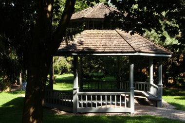 Açık gri kiremitleri olan açık gri bir çardak. Önünde ağaç olan kiremitler. Shafe dökülüyor.