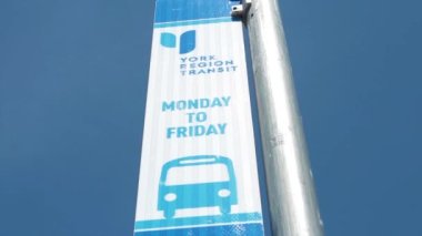 New York bölgesi transit taşımacılığı Pazartesi 'den Cuma otobüsü tabelasına sağ çerçeve çerçevesi üzerinde, açık gökyüzü arkasında gümüş metal direği ile mavi baskı, sola kayma hareketi
