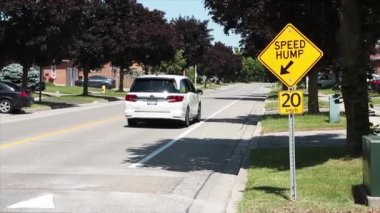 Hız hörgücü okunda orta hız 20 km / saat işareti sarı arka plan gümüş direğinde siyah yazıyla hız tümseğinin üzerinden geçen arabalar