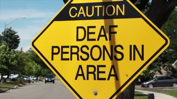 エリア内の聴覚障害者に注意してください長い通りと背景に通過するぼやけた車と黄色の背景に黒い文字でダイヤモンドの看板 — ストック動画