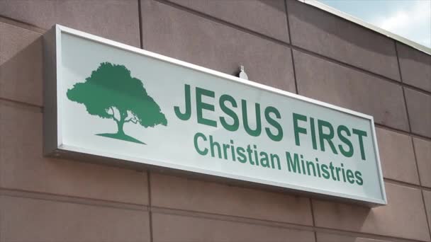 イエス第一キリスト教のミニストリーは木の絵と建物の壁の絵と緑の文字で長方形のサインを 角度で撮影 — ストック動画